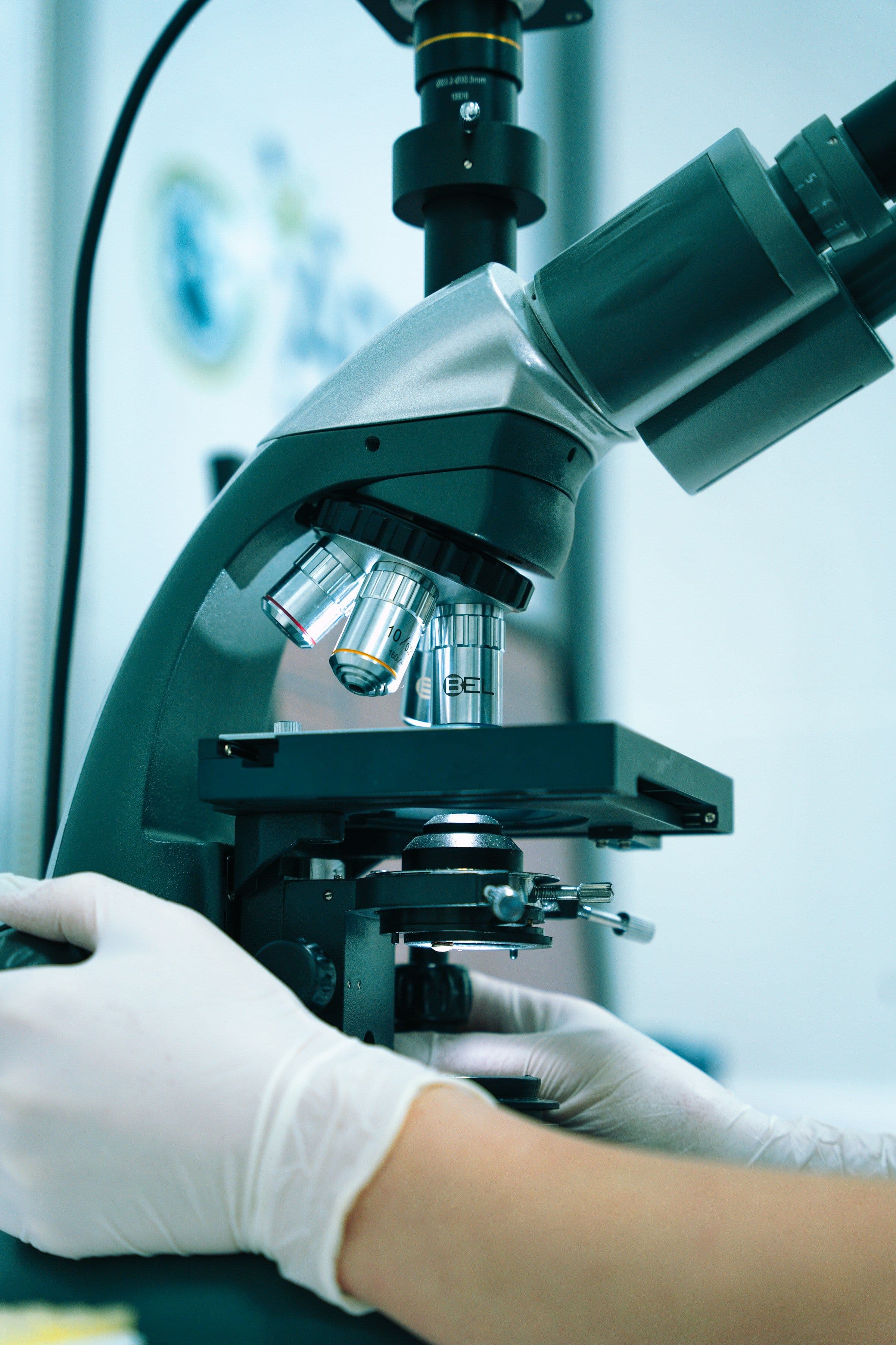 A gloved hand operating a microscope in a laboratory